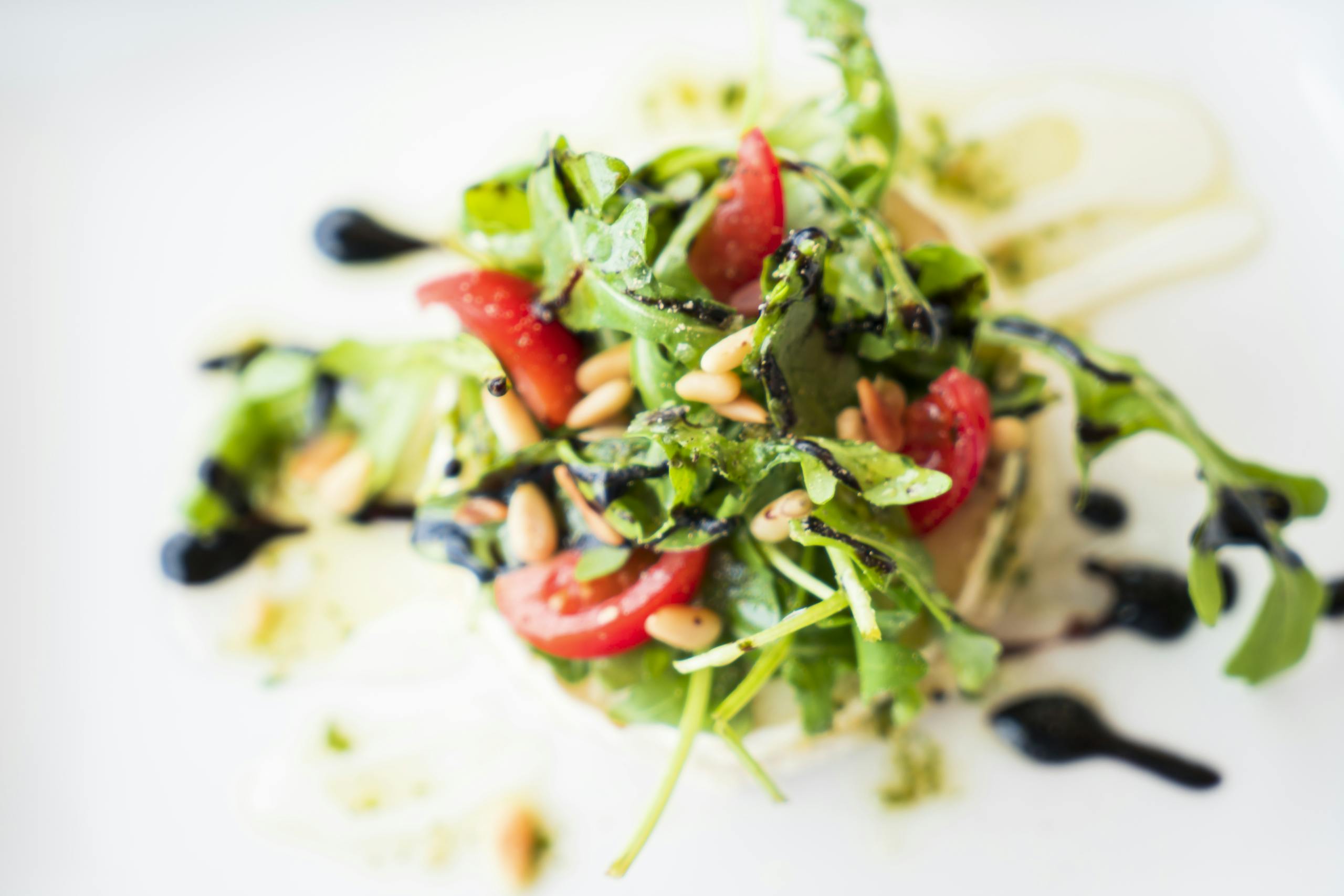 A vibrant arugula salad with cherry tomatoes, pine nuts, and balsamic glaze.